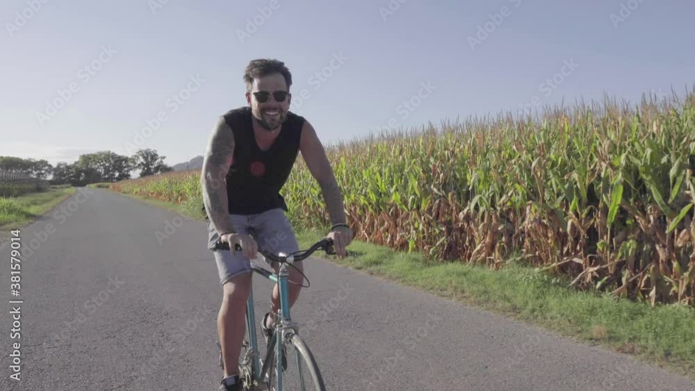 Cheerful man riding bicycle along rural field Cheerful man riding bicycle along rural field