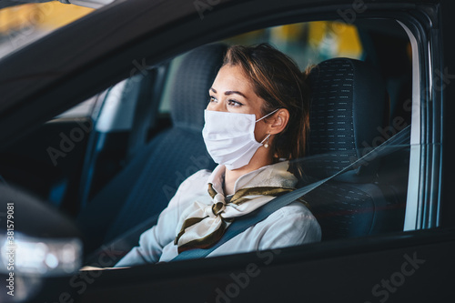 Young handsome fashionable businesswoman with protective face mask on driving herself on work during corona virus outbreak.