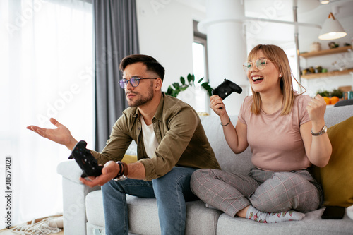 Boyfriend and girlfriend playing video game with joysticks in living room. Loving couple are playing video games at home...