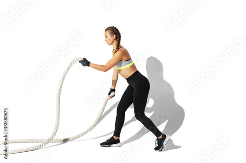 Ropes. Beautiful young female athlete practicing on white studio background, portrait with shadows. Sportive fit model in motion and action. Body building, healthy lifestyle, style concept.