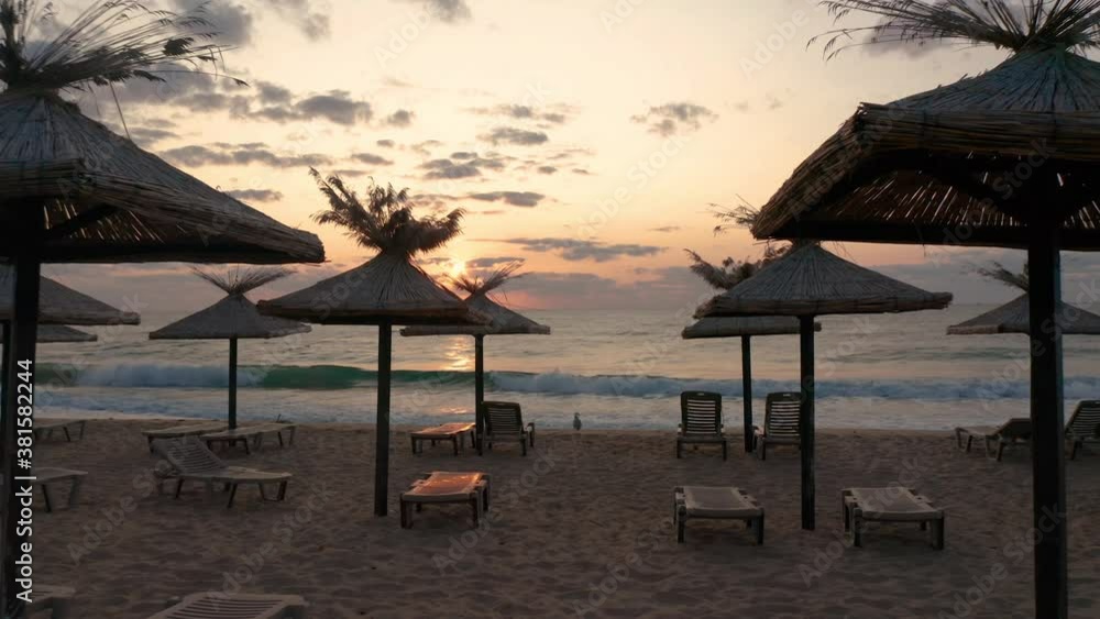 Video with straw sunshades and sunbeds on an empty sandy beach at sunrise Video with straw sunshades and sunbeds on an empty sandy beach at sunrise