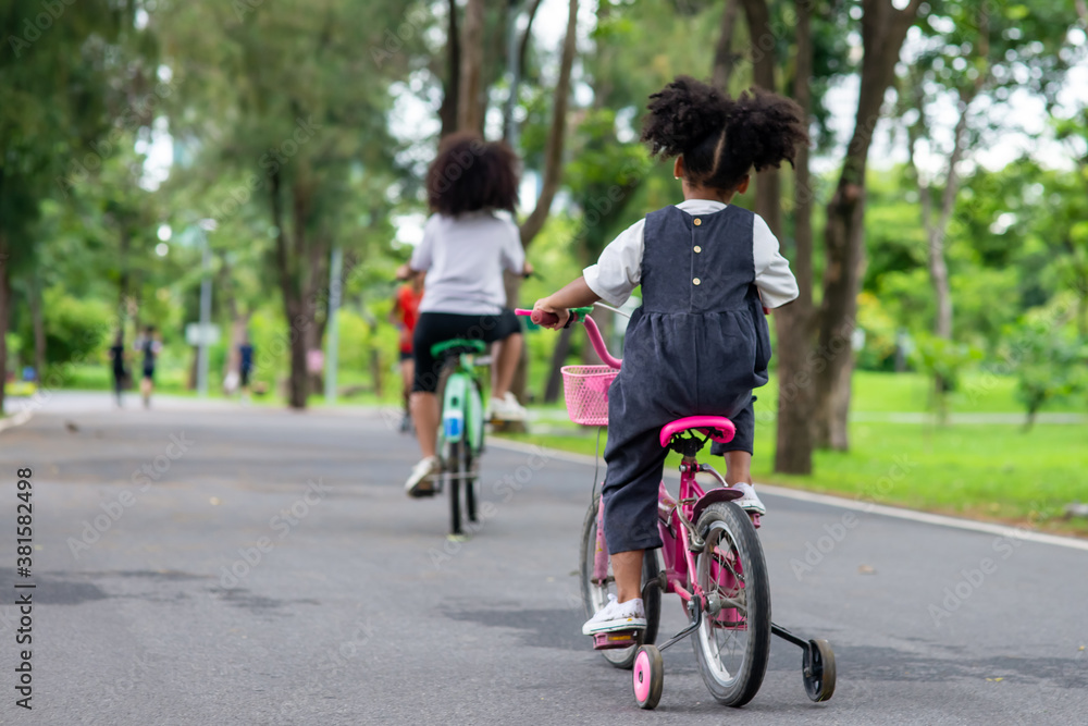 Happy affectionate mixed race family. Two little cute child girl sister  riding bicycle together in the park. Adorable sibling enjoy and having fun learning ride a bike in outdoor weekend vacation.