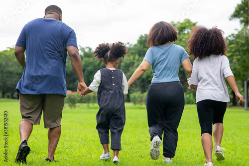 Happy mixed race family parents with cute child girl holding hands and walking together in the park. Father and mother with two daughter enjoy and having fun in summer outdoor holiday vacation.