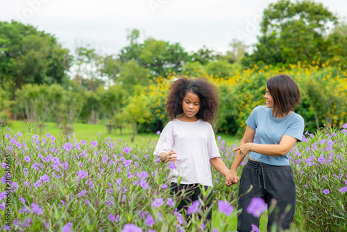 Happy mixed race family mother with little daughter holding hands and walking together in the garden. Smiling mom with cute child girl  enjoy and having fun in summer outdoor weekend holiday vacation