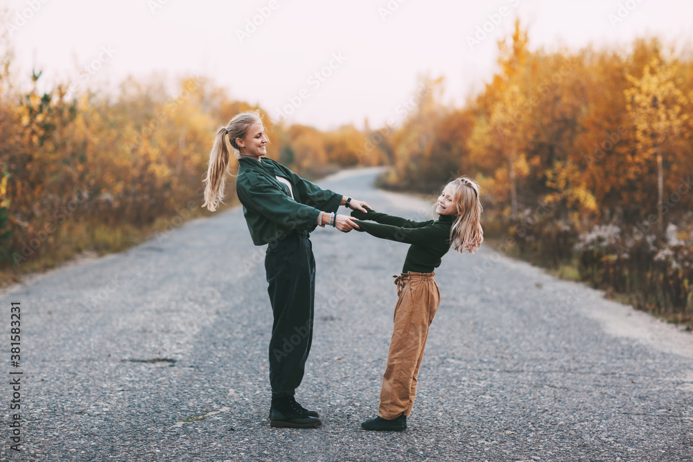 Obraz premium Happy mature mom and her blonde little daughter hugging and laughing while walking in autumn park outdoors