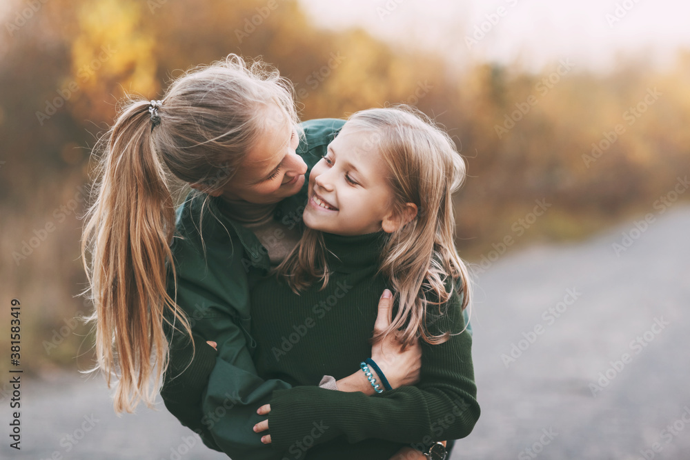 Portrait of happy mature mom and her blonde little daughter hugging and laughing while walking in autumn park outdoors. Portrait of happy mature mom and her blonde little daughter hugging and laughing while walking in autumn park outdoors.