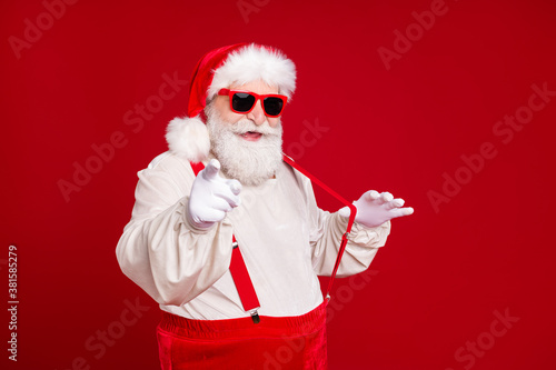 Portrait of his he nice handsome cheerful cool content bearded fat Santa pulling suspenders pointing at you having fun invite celebratory isolated bright vivid shine vibrant red color background