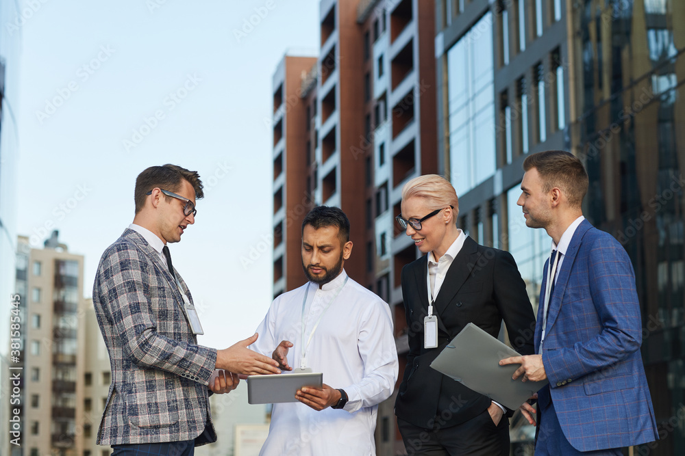 Businessman using digital tablet and discussing online presentation with his colleagues while they standing in the city outdoors Businessman using digital tablet and discussing online presentation with his colleagues while they standing in the city outdoors
