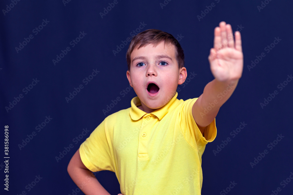 Little open mouth 9s boy putting his hand out making stop sign gesture.Blue studio wall Little open mouth 9s boy putting his hand out making stop sign gesture.Blue studio wall