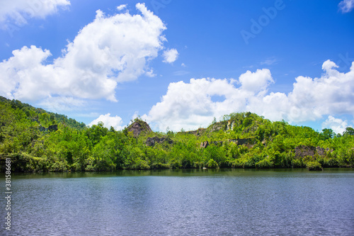 Blue sky with clouds, mountain covered with many trees and lake in front of them. © nut_foto