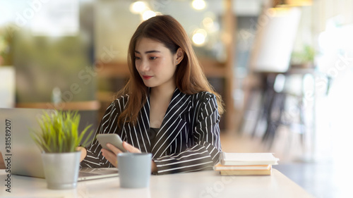 Portrait of female office worker looking on laptop while holding smartphone