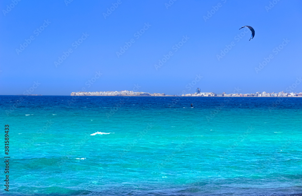 Kite surfing on the sea: on background Gallipoli skyline, Apulia (Italy), whose name means Beautiful City, rests like a mirage on the Ionian coast, roughly 40 km from Lecce. Kite surfing on the sea: on background Gallipoli skyline, Apulia (Italy), whose name means Beautiful City, rests like a mirage on the Ionian coast, roughly 40 km from Lecce.