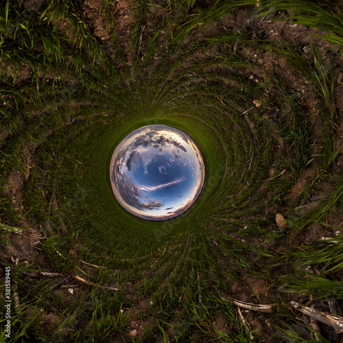 Inversion of blue tiny planet transformation of spherical panorama 360 degrees. Spherical abstract aerial view on field with awesome beautiful clouds. Curvature of space.