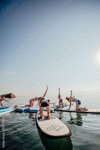 Young woman doing Pilates on a SUP board in the lake at sunrise