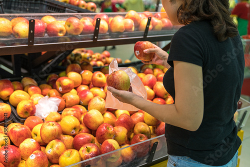 Hands of female buyer choosing red apples in supermarket