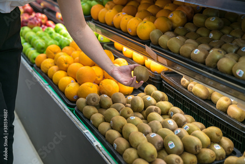 Fresh healthy fruits on shelves in supermarket. With a woman hand choosing best fruits