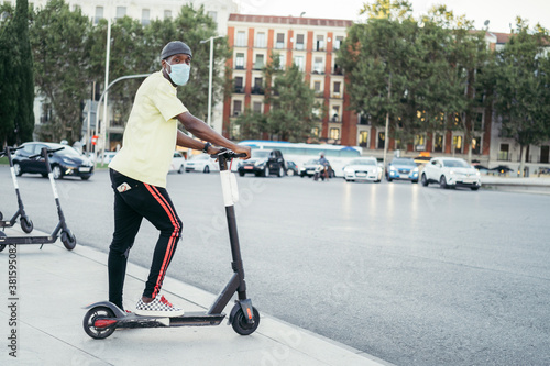 Black man with surgical mask looking to camera on electric scooter