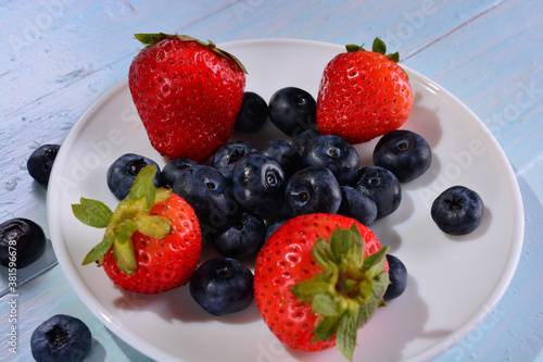 strawberries and blueberries on a white plate on a blue wooden table background. concept of fresh and healthy food  harvesting.