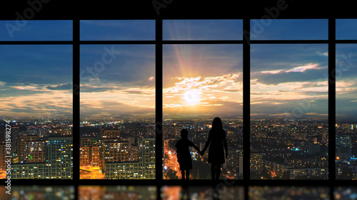 The boy and girl standing near the panoramic window against the beautiful sunset