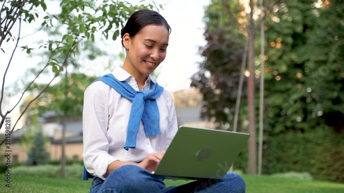 Cheerful asian woman using her laptop outdoors
