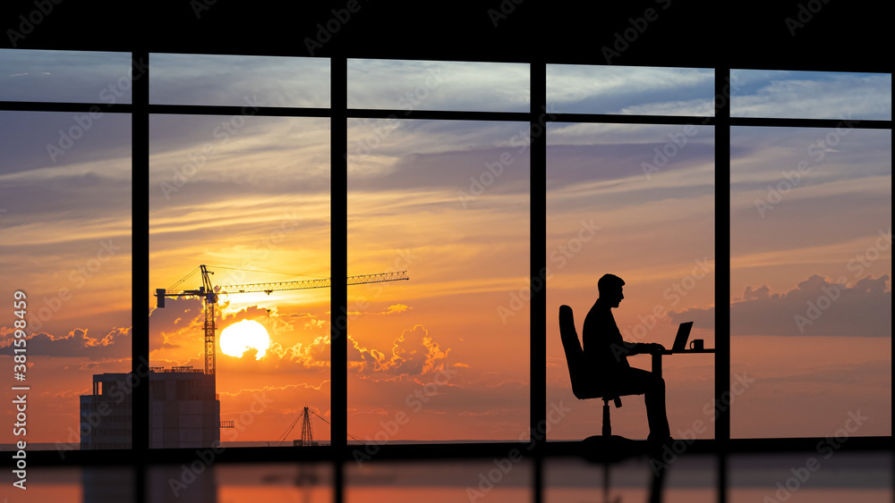The businessman sitting near a panoramic window against the city sunset
