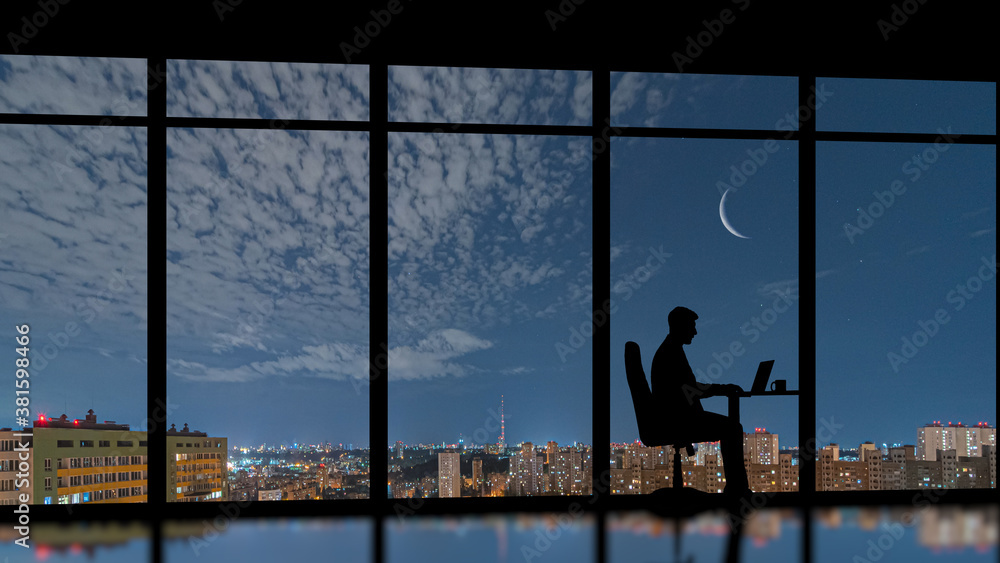 The businessman sitting near the panoramic window on the night city background The businessman sitting near the panoramic window on the night city background