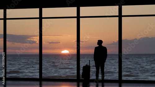 The man with a suitcase standing near a panoramic window against the sea sunset © realstock1