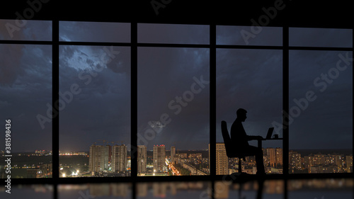 The businessman sitting near a panoramic window with a night city background