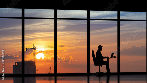 The businessman sitting near a panoramic window against the city sunset