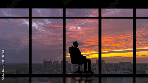 The man sitting near the panoramic window against the city sunset