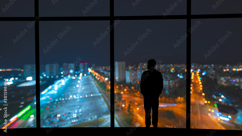 The man standing near the panoramic window against the night city The man standing near the panoramic window against the night city