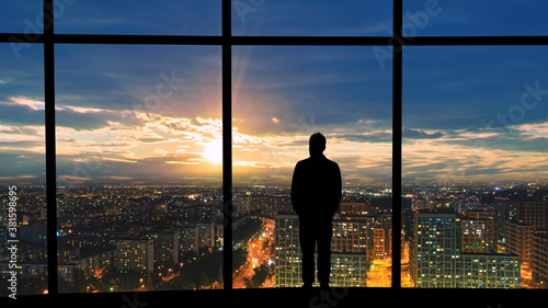 The male standing near the panoramic window against the beautiful sunset