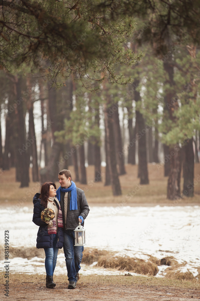 couple on winter walk in snow. Valentine's Day  for couple in rustic style. Happy couple in love warming themselves with tea under a blanket in the arms of nature. Casual outfit with Blue accessories