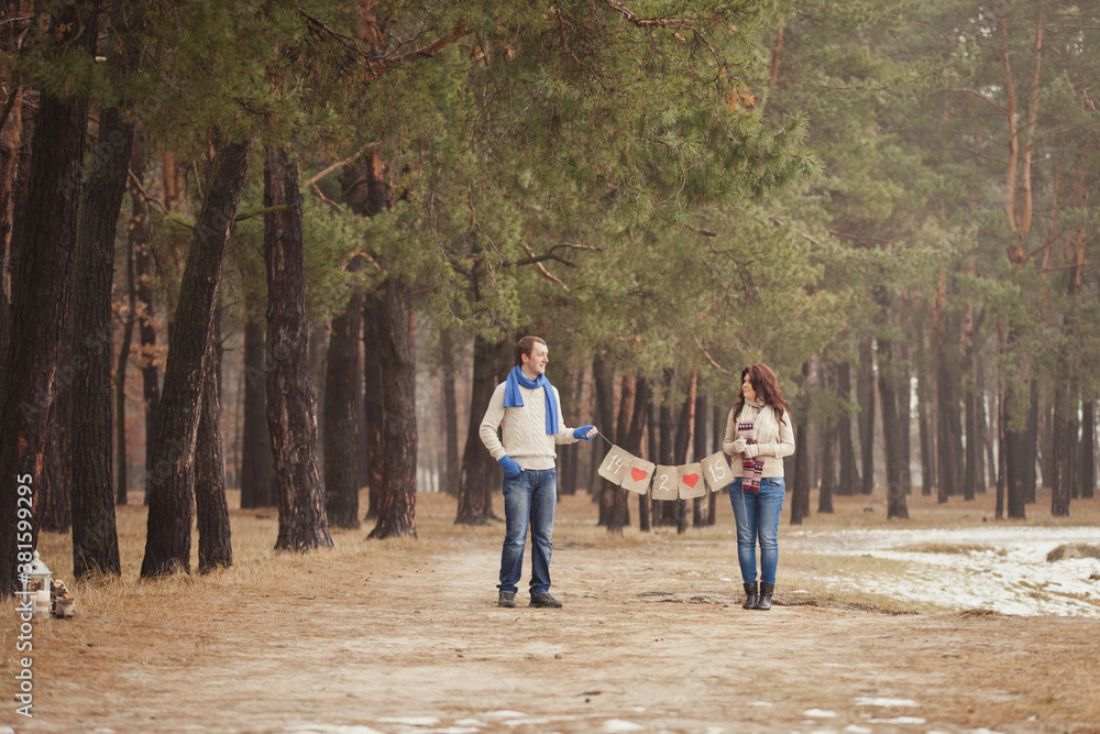 couple on winter walk in snow. Valentine's Day for couple in rustic style. Happy couple in love holding garland flags with inscription 14 February in their arms. Casual outfit with Blue accessories couple on winter walk in snow. Valentine's Day for couple in rustic style. Happy couple in love holding garland flags with inscription 14 February in their arms. Casual outfit with Blue accessories