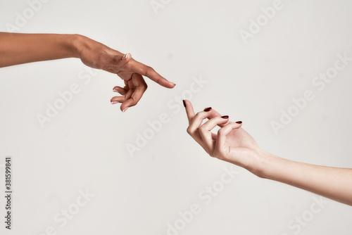 Close up of two hands of diverse women reaching for each other isolated over grey background
