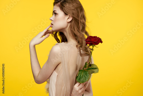 Romantic girl on a yellow background with a red flower in her hand and an evening dress model