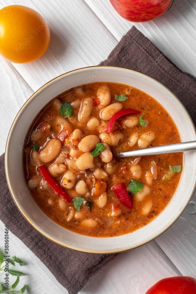 Bulgarian Bean Soup - Bob Chorba, tomatoes, bread and mint on white wooden table. Vertical orientation. Flat lay. Close up. Bulgarian Bean Soup - Bob Chorba, tomatoes, bread and mint on white wooden table. Vertical orientation. Flat lay. Close up.