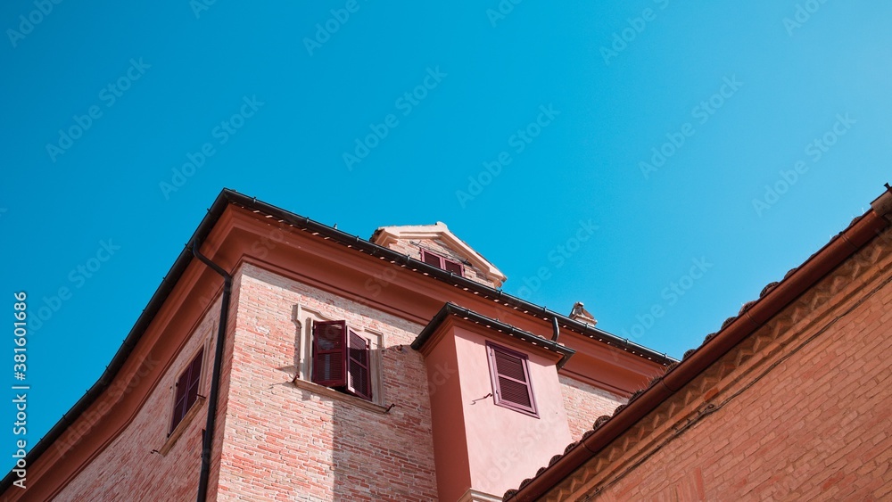 A brick facade of an old building with windows and shutters above the roof (Corinaldo, Marche, Italy, Europe)