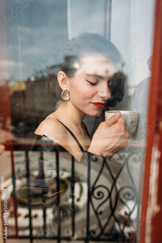 young beautiful woman with a cup of fragrant coffee standing by the window