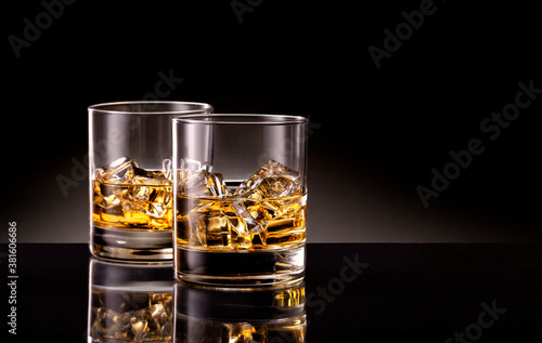 Two glasses of whiskey with ice cubes on black background.