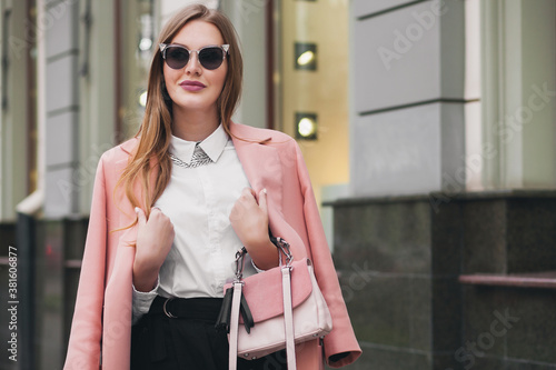 attractive stylish smiling rich woman walking city street in pink coat spring fashion trend holding purse, elegant style, wearing sunglasses