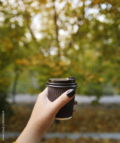Hand with cup of coffee on autumn background.