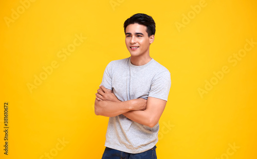 Handsome young Asian man smiling and arms crossed over yellow background.