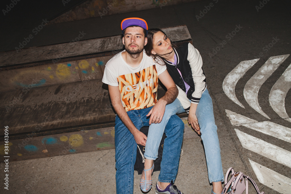 cool young stylish hipster couple in love, swag outfit, jeans, embrace, cool accessories, sitting happy, having fun
