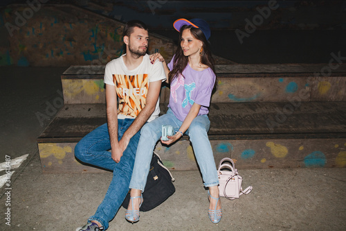 cool young stylish hipster couple in love, swag outfit, jeans, embrace, cool accessories, sitting happy, having fun