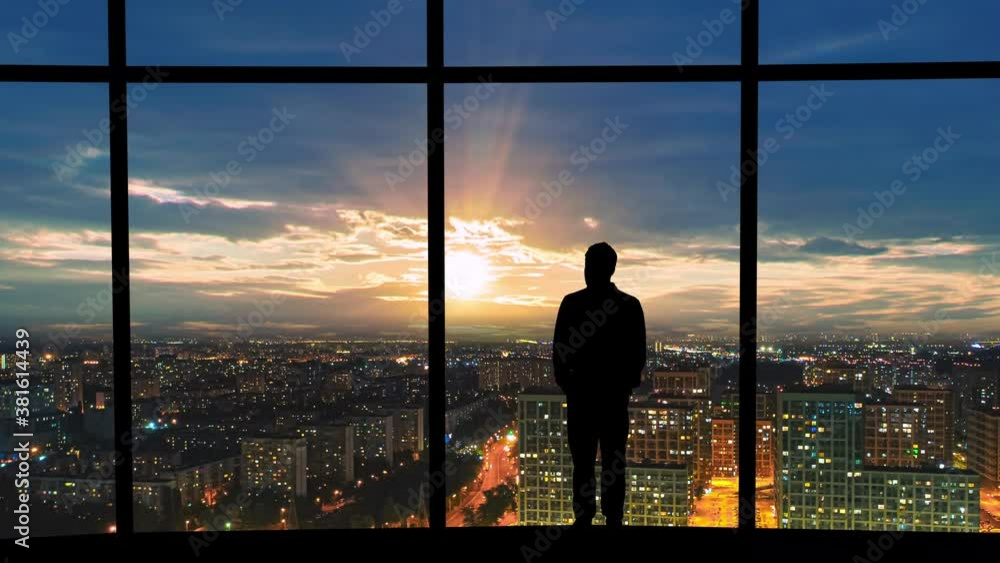 The man is standing near the windows on the night urban background. time lapse