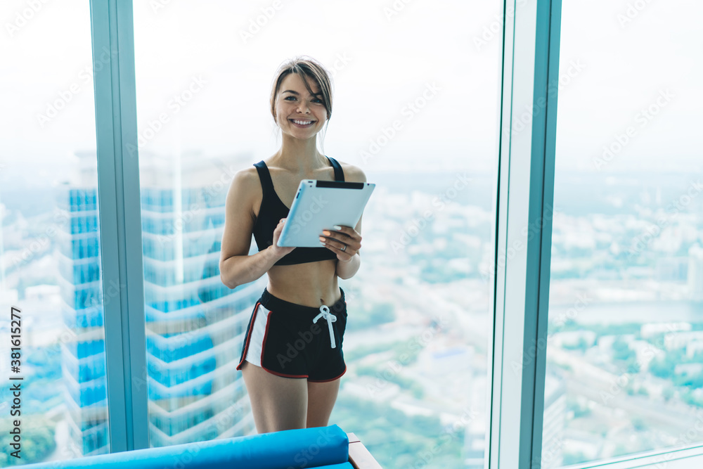 Half length portrait of beautiful slim woman in activewear holding modern digital tablet for blogging, cheerful hipster girl sending mails and communicating via tablet connected to 4G internet