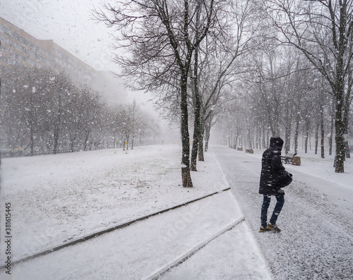 A man walks in snowy weather on the Boulevard. Heavy snowfall, walking with the dog. Thick snow covered trees, streets, and people. Snow storm, Blizzard.in the city. People under thick large snowflake