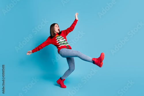 Full body size photo of cute pretty lady stand tiptoe raise hands funny falling open mouth terrified mad look empty space wear red sweater jeans boots isolated blue color background