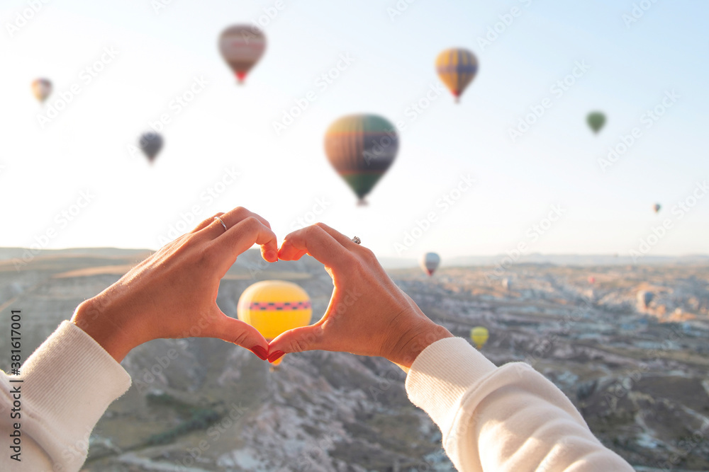 Fototapeta premium Women's hands in the shape of a heart against the background of flying balloons in the sky of Cappadocia. Holidays in Turkey, travel during a pandemic